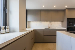 INKO Cocinas: cocina moderna de líneas rectas en gris cálido, encimera de mármol blanco, fregadero y grifo dorado, electrodomésticos empotrados.