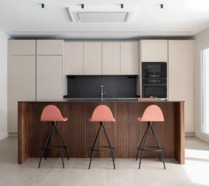 INKO Cocinas, cocina de diseño moderno con isla de madera ribeteada, encimera negra y electrodomésticos empotrados; asientos rosas elegantes.