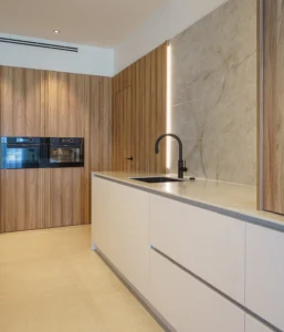 INKO Cocinas cocina contemporánea con muebles de madera cálida, encimera clara, isla con fregadero y grifo negro, hornos empotrados.