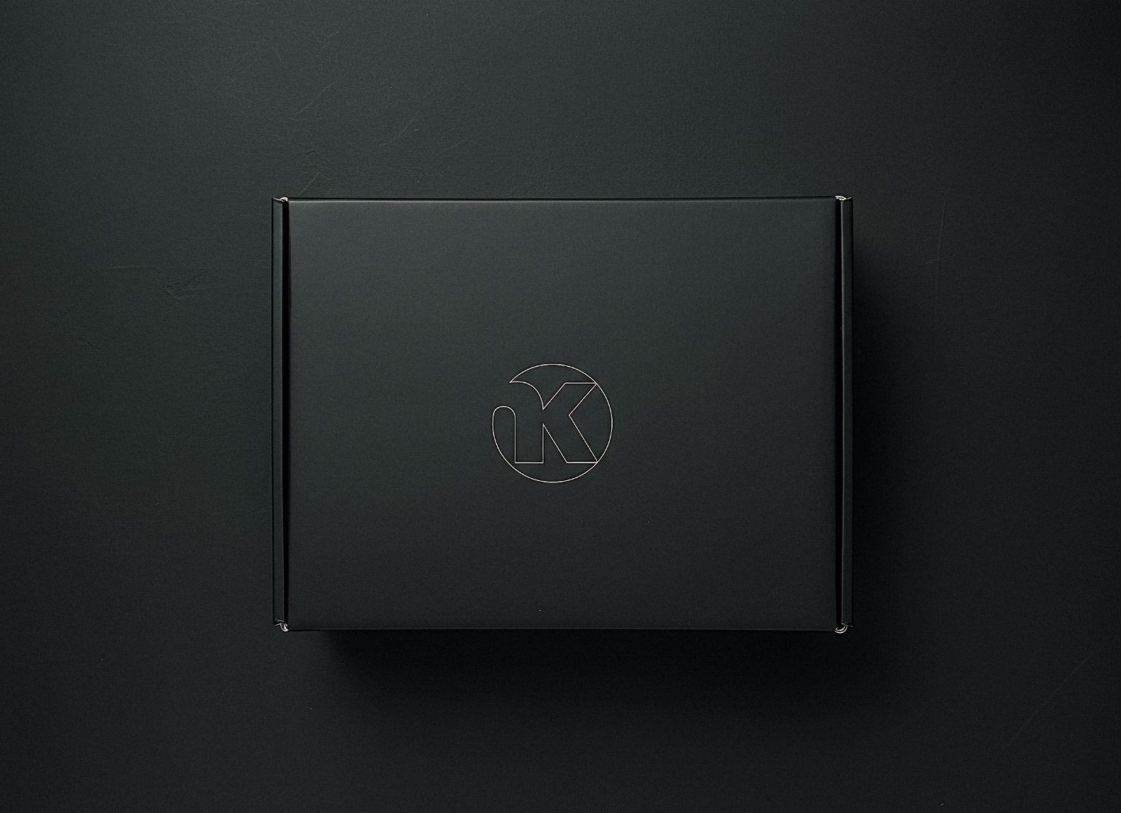 Caja negra rígida con logotipo circular minimalista que integra las letras OK; packaging premium y diseño sobrio. INKO Cocinas
