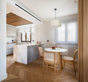 INKO Cocinas: cocina contemporánea de diseño premium con isla de mármol, encimeras blancas y comedor circular con paneles de madera.