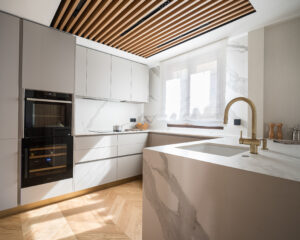 INKO Cocinas: cocina moderna de diseño premium con luz natural, encimeras de mármol, gabinetes blancos y isla con grifo dorado.