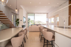 INKO Cocinas diseño de cocina premium en planta abierta: isla blanca, taburetes beige, iluminación moderna y vistas al exterior.