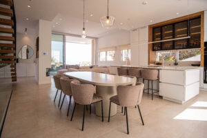 Espaciosa cocina y comedor de diseño premium con isla blanca, mesa ovalada y sillas beige, iluminación moderna. INKO Cocinas
