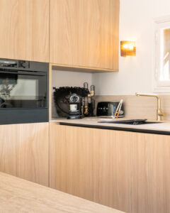 INKO Cocinas cocina moderna de madera clara con horno empotrado, cafetera, tostadora y grifo dorado; diseño premium.
