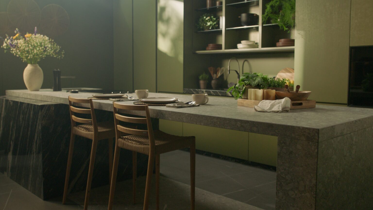INKO Cocinas, isla de cocina en piedra gris con taburetes de madera, estanterías con platos y plantas; diseño premium en Málaga