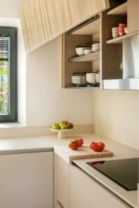 INKO Cocinas: cocina moderna de diseño premium con muebles beige, estantería abierta y encimera clara; tomates en la tabla junto a la ventana.