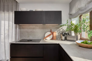 INKO | Fabricantes de Cocinas en Málaga y Diseño a Medida | Cocina moderna con armarios negros y encimera gris, iluminación suave y planta; diseño premium INKO Cocinas