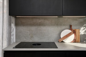INKO | Fabricantes de Cocinas en Málaga y Diseño a Medida | INKO Cocinas: cocina contemporánea con gabinetes negros, encimera de concreto y placa de inducción; tablas de madera y iluminación LED.