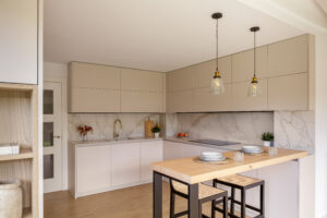 Cocina moderna en lacado beige con isla de madera natural, salpicadero de mármol, iluminación cálida y líneas rectas – INKO Cocinas