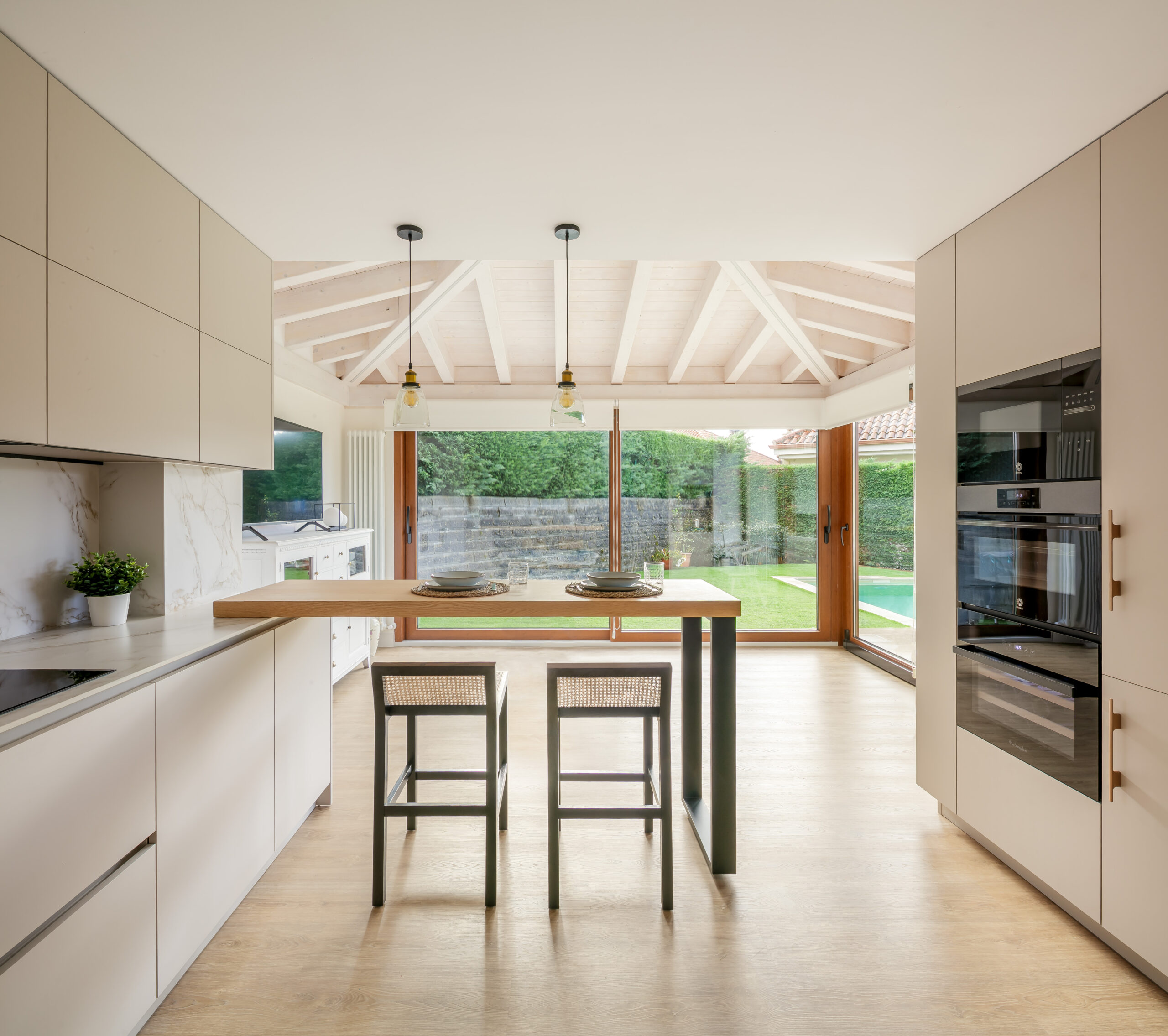 Cocina moderna minimalista en lacado blanco mate con isla y barra en madera, encimera de piedra y iluminación cálida – INKO Cocinas