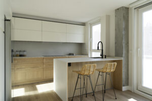 INKO | Fabricantes de Cocinas en Málaga y Diseño a Medida | INKO Cocinas cocina de diseño premium con armarios blancos y base de madera, isla con encimera clara, grifo negro y taburetes de mimbre.