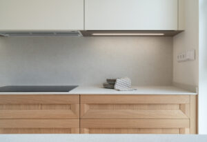 INKO | Fabricantes de Cocinas en Málaga y Diseño a Medida | INKO Cocinas - Cocina moderna con encimera clara y muebles de madera, placa de inducción, vajilla y paño a cuadros, diseño premium