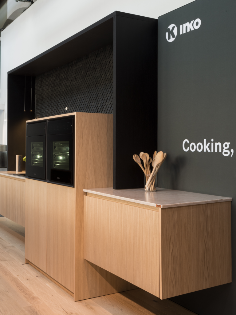 INKO | Fabricantes de Cocinas en Málaga y Diseño a Medida | INKO Cocinas: mostrador de cocina premium con madera clara, hornos empotrados y backsplash negro; Diseño de cocinas a medida en Málaga